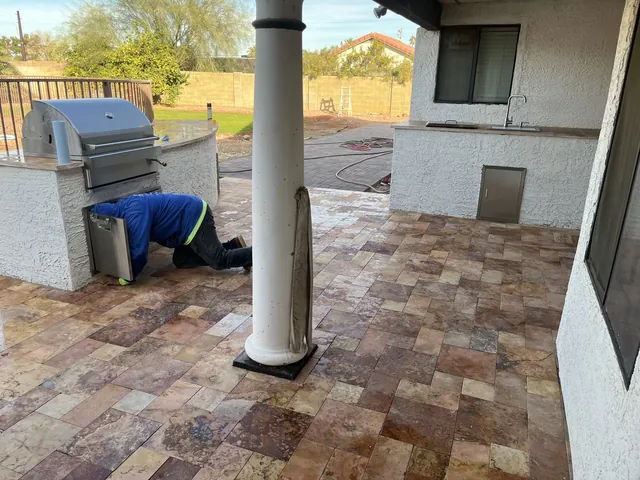 Travertine patio around a white column with a built-in grill, as a crew member works on the outdoor kitchen