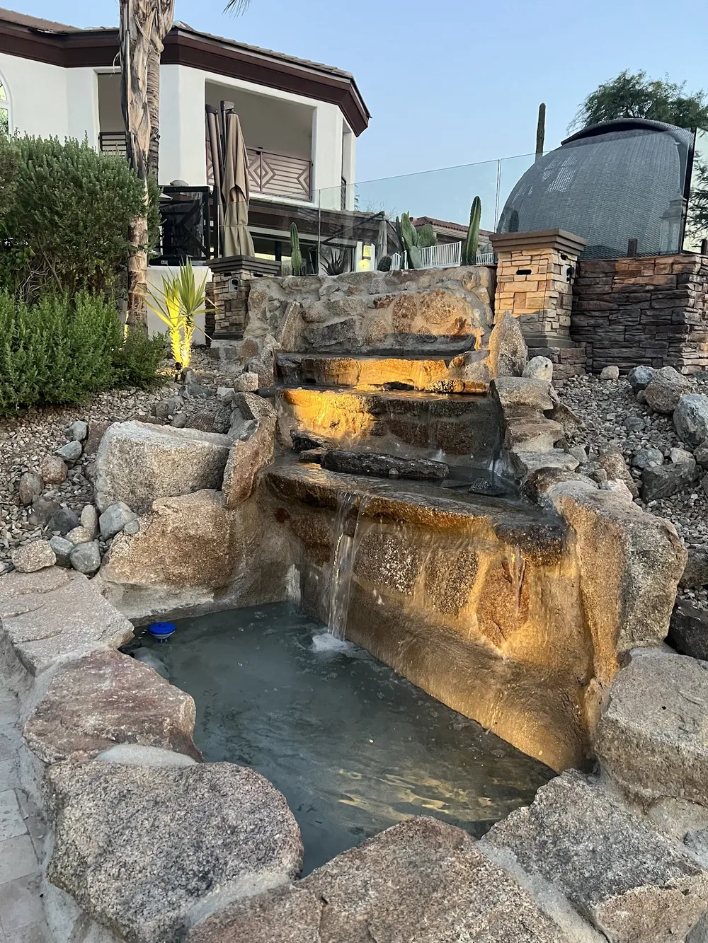 Boulder waterfall with lights built into the rocks, feeding a pond beside a patio