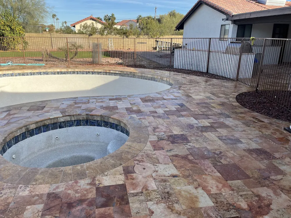 Travertine pool deck wrapping a spa, with a wrought-iron pool fence and neighboring homes behind