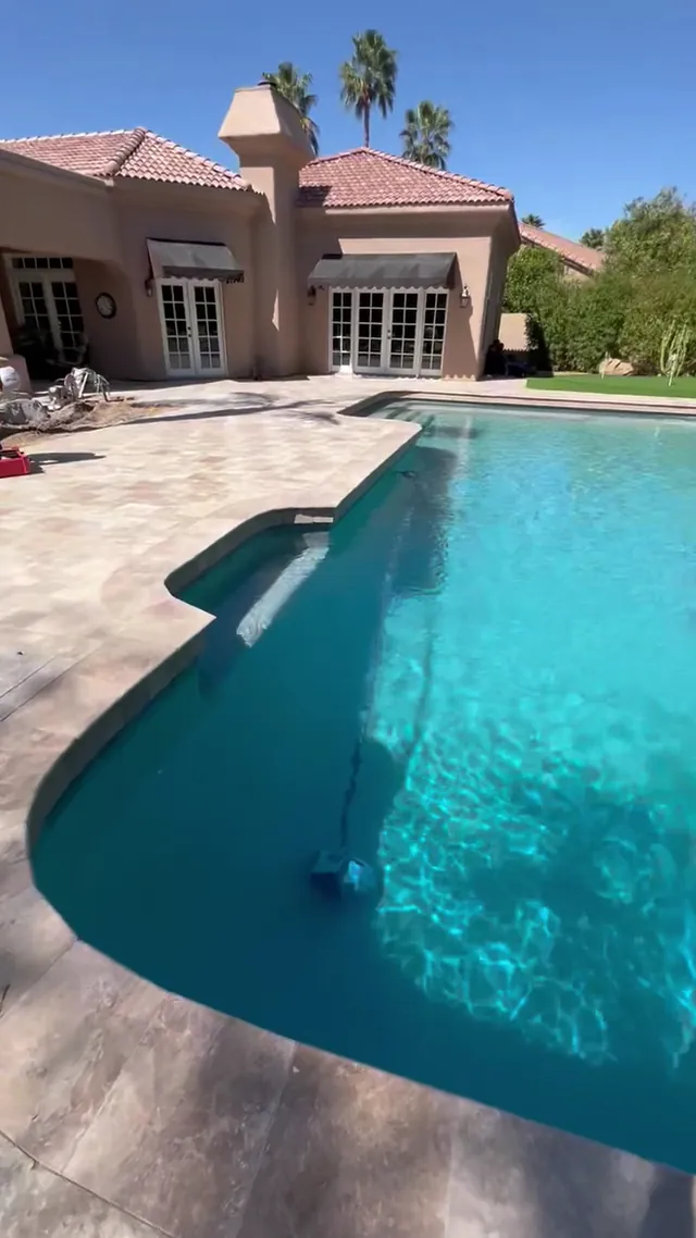 Backyard pool with a long travertine paver deck beside a stucco home