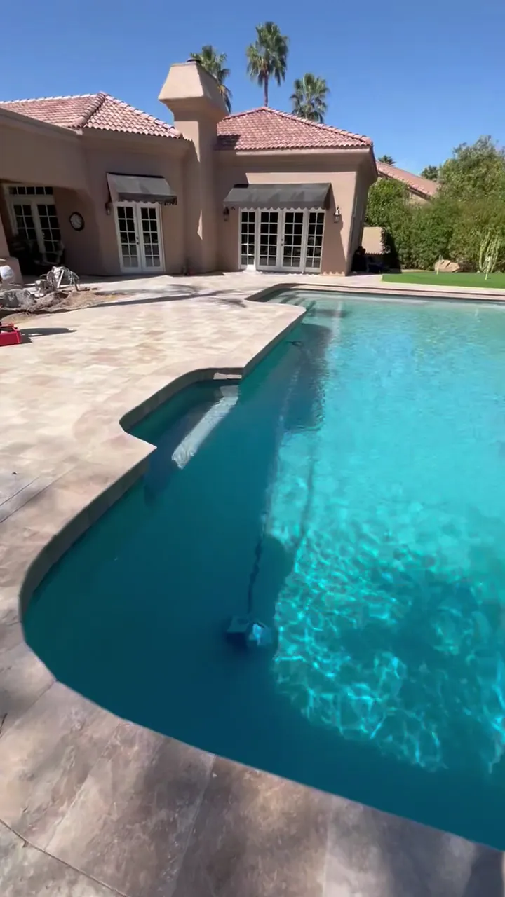 Backyard pool with a long travertine paver deck beside a stucco home