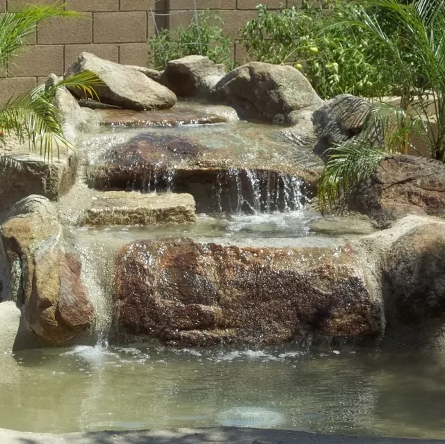 Small boulder waterfall dropping into a pond with palms planted behind it